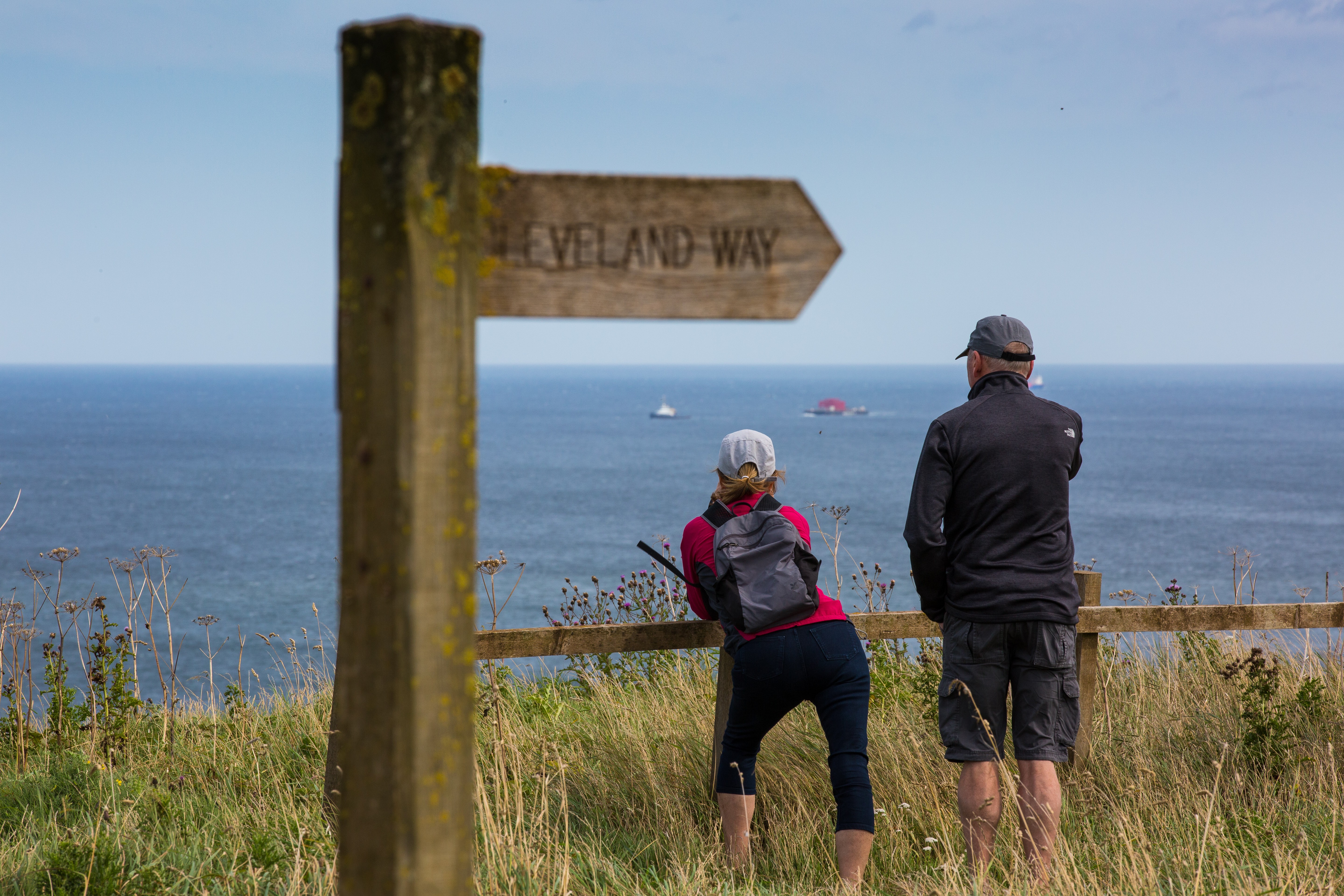 Couple leaning over fence looking out to sea with Cleveland Way signpost